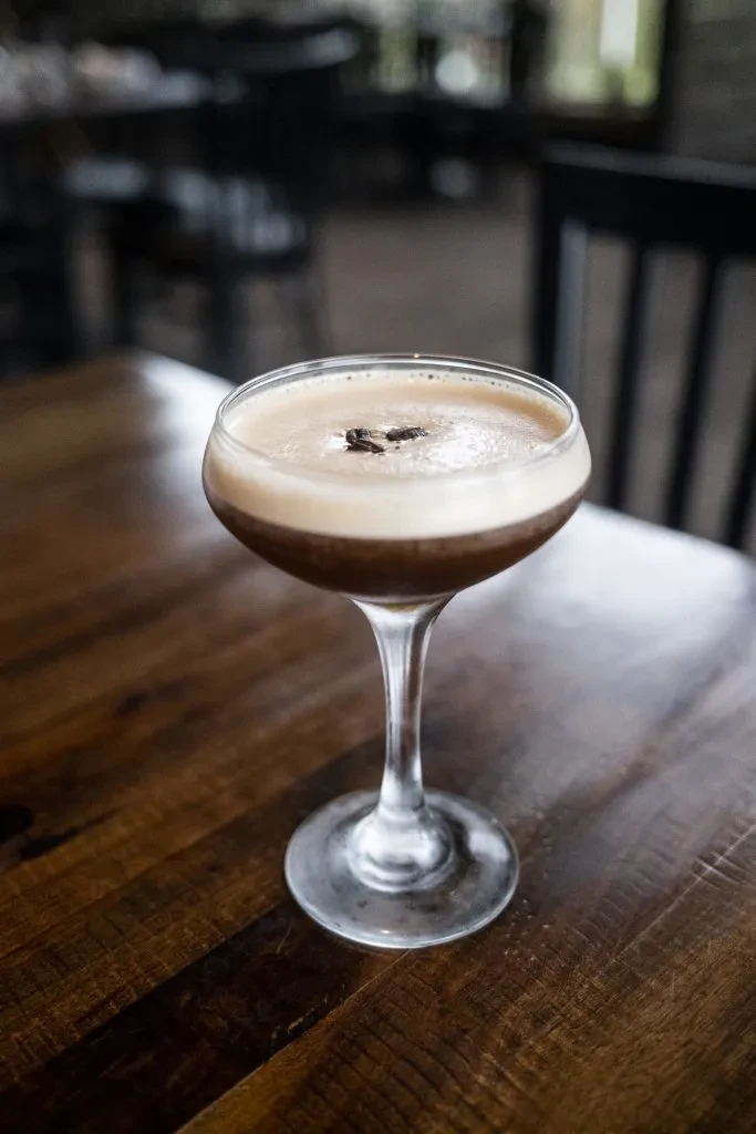 Coupe glass with a dark brown drink, foam, and three coffee beans.