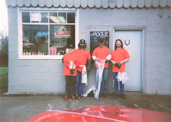 Four people in orange shirts with plastic bags outside Henry's Pizza.