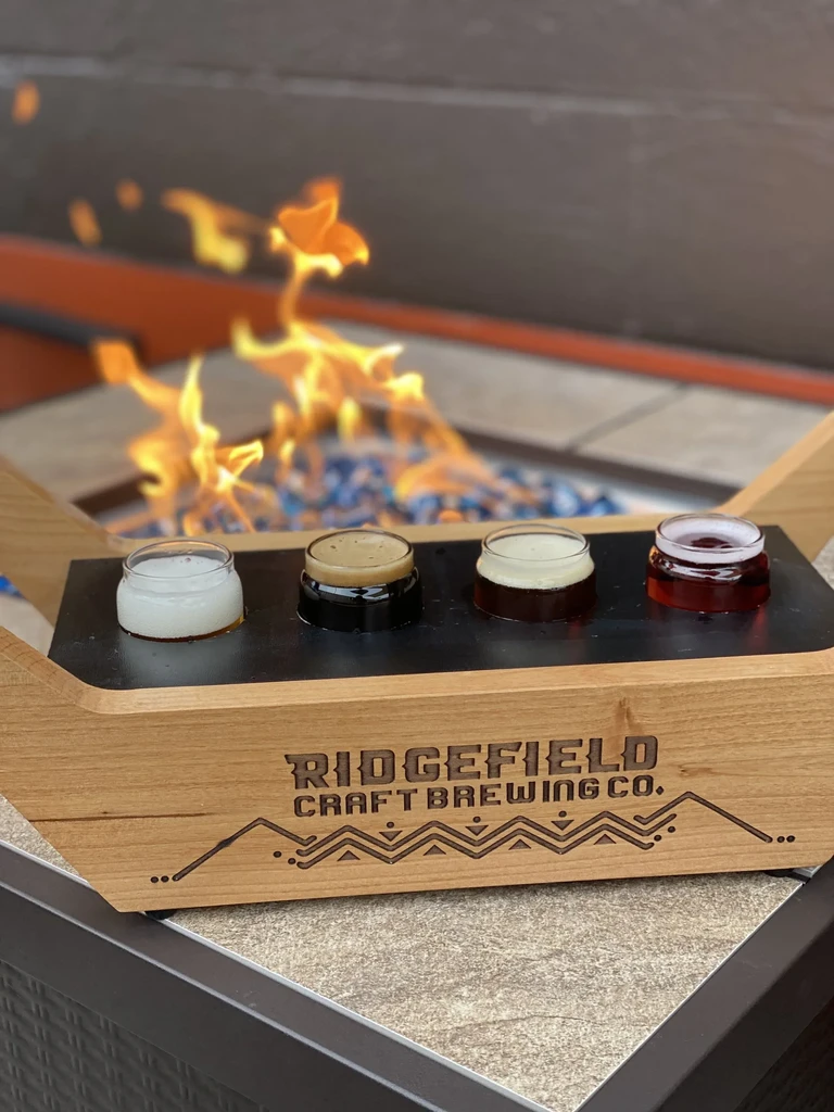 Flight of four Ridgefield Craft Brewing beverages on a paddle by a fire pit.