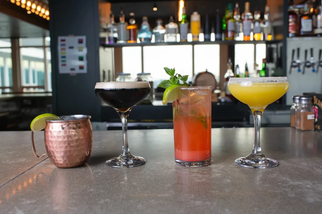 Four distinct cocktails on a bar counter with a stocked bar.