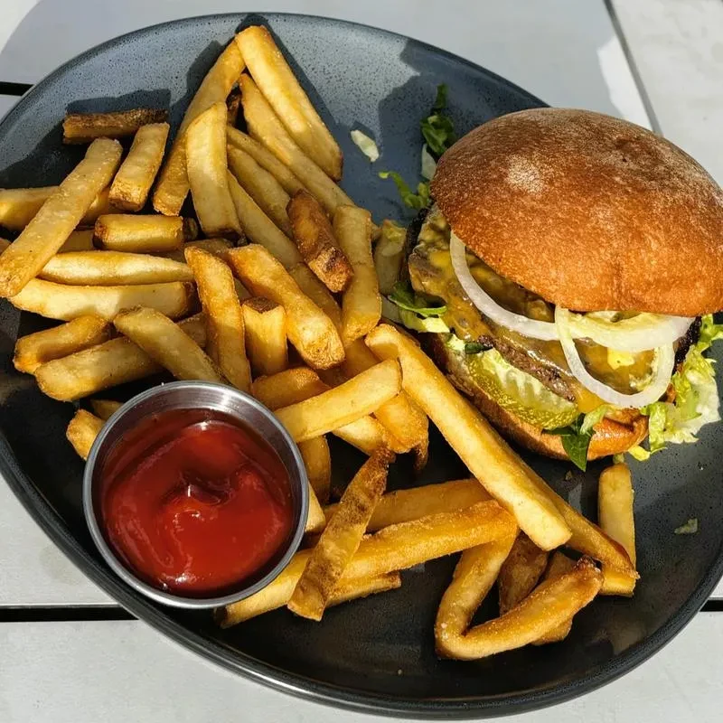 Classic burger, golden fries, and ketchup served on a dark plate.