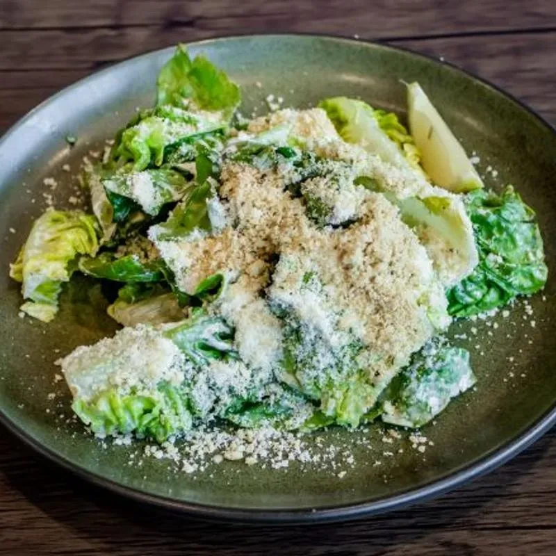 Overhead Caesar salad with romaine, creamy dressing, Parmesan, breadcrumbs, lemon.