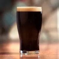Pint glass of dark beer, topped with a thick, creamy head.