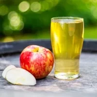 Glass of apple juice, whole apple, and slices on wood outdoors.