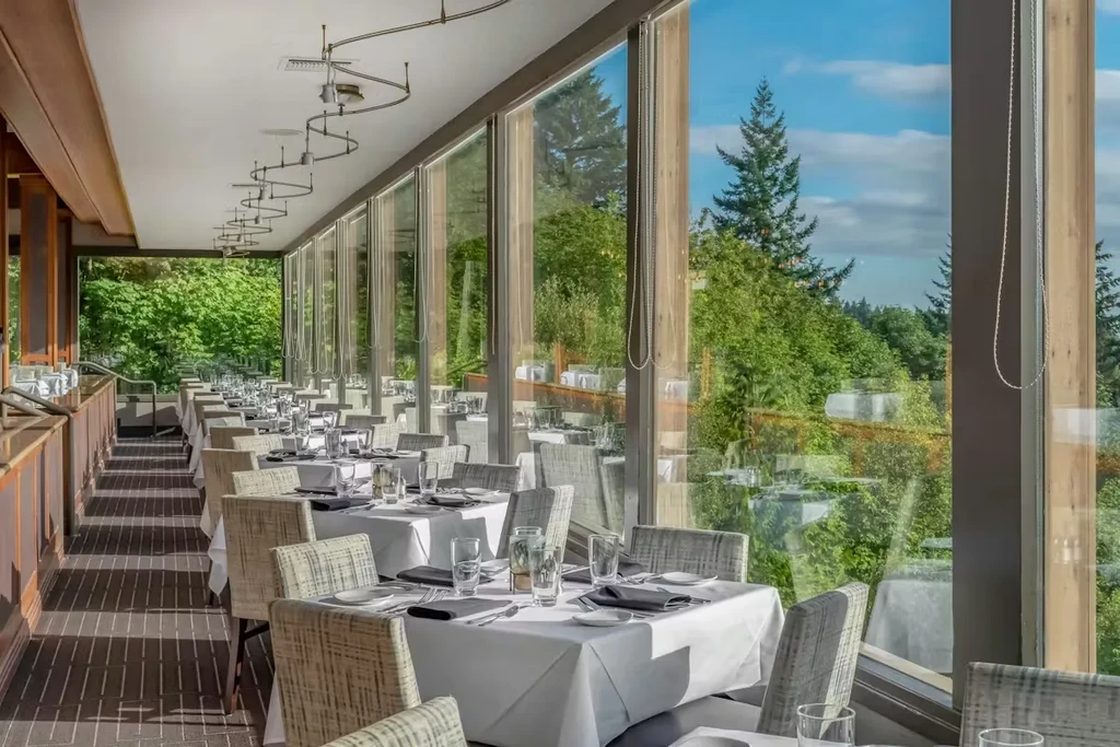 Modern restaurant dining room with floor-to-ceiling windows and nature view.