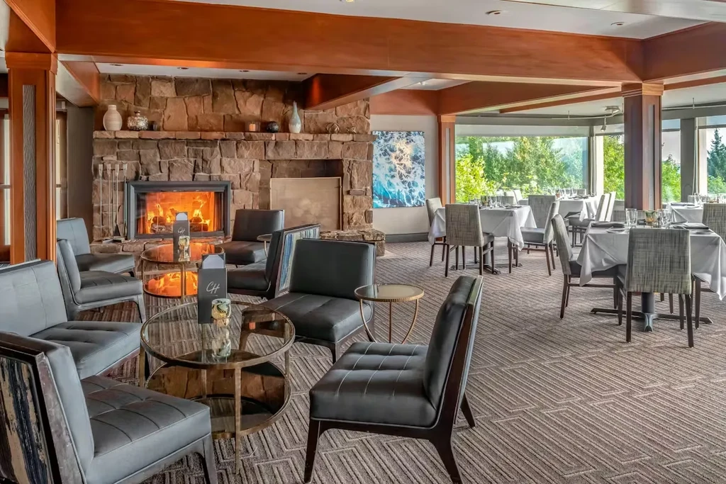 Sophisticated restaurant interior with fireplace lounge and green tree views.