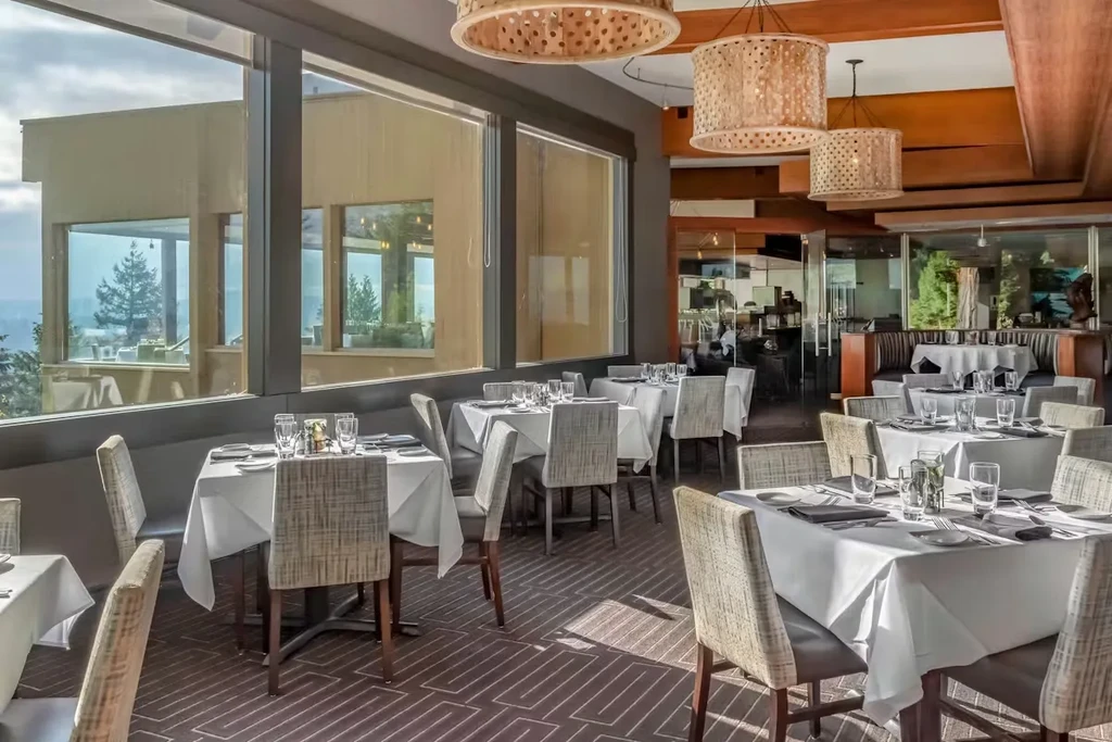 Upscale restaurant dining room with set tables, natural light, and scenic view.