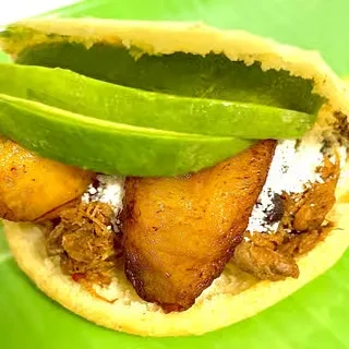 Open cornmeal patty with shredded meat, avocado, plantain, and cheese.