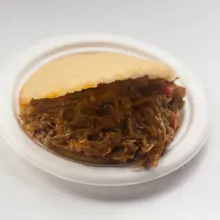 Close-up of arepa filled with shredded meat and dark sauce.