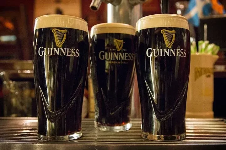 Three dark Guinness pints with creamy white heads on a bar.