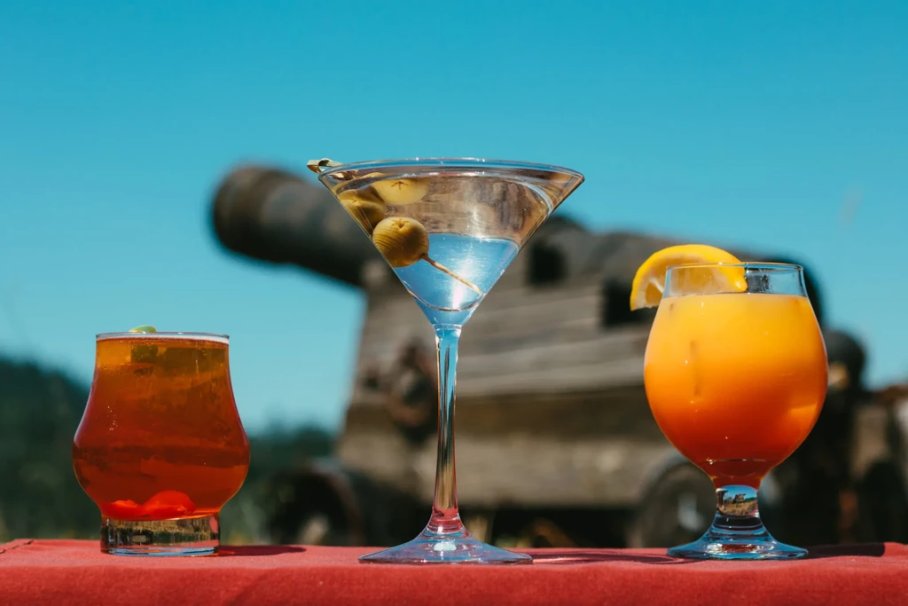 Three diverse drinks on a red tablecloth, blurred cannon background.
