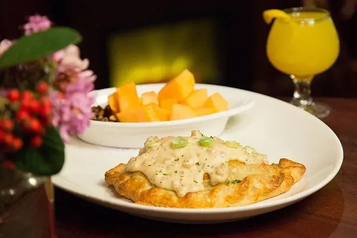 Biscuit and gravy, diced fruit, and yellow drink on a table.