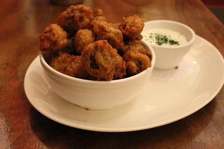 Crispy fried mushrooms with herbed dipping sauce on a rustic wooden table.