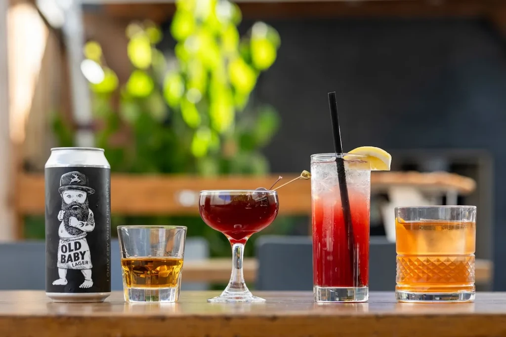 Four distinct alcoholic beverages on a wooden table outdoors.