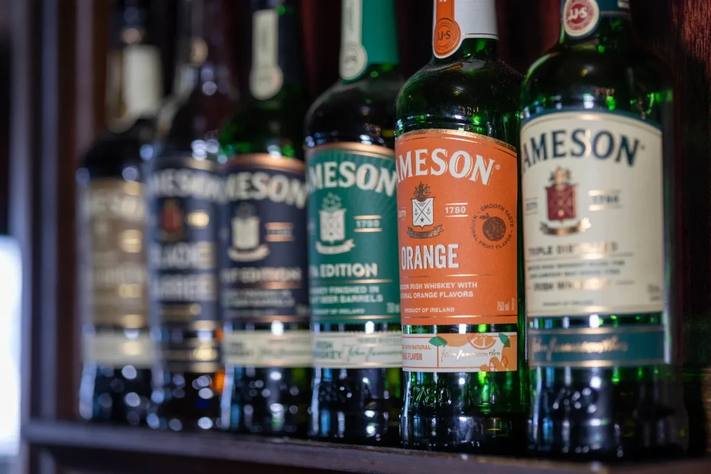 Close-up of various Jameson Irish Whiskey bottles on a wooden bar shelf.