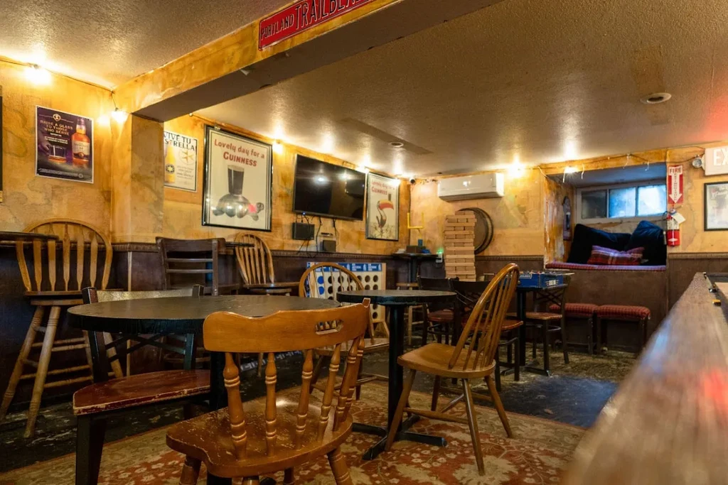 Empty rustic pub interior with warm lighting, wooden chairs, and posters.