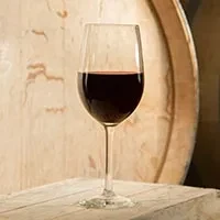 Clear glass of red wine on wood with blurred wine barrel.
