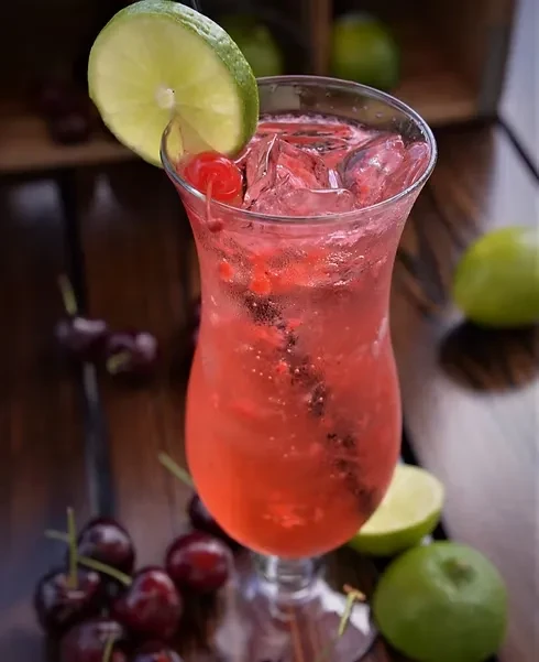 Red-pink bubbly drink in fluted glass with cherry and lime.