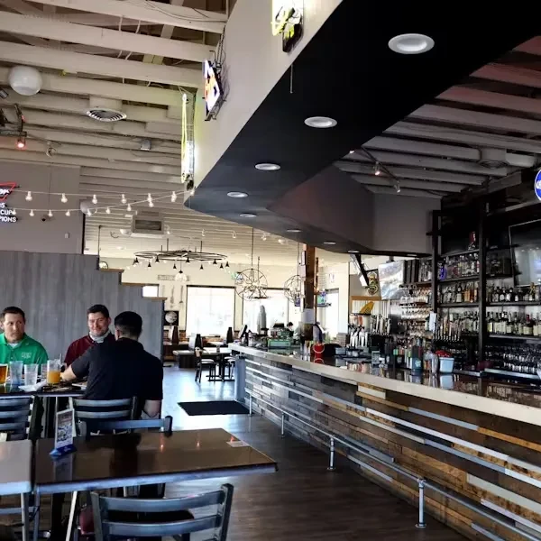 Casual restaurant bar with wooden counter, liquor, beer taps, and seated diners.