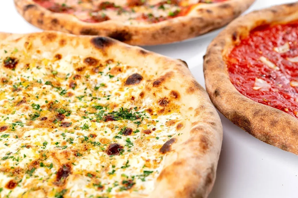 White pizza with herbs in front of two red-sauce pizzas.