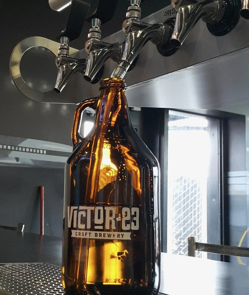 VICTOR-23 CRAFT BREWERY growler being filled from chrome beer taps.