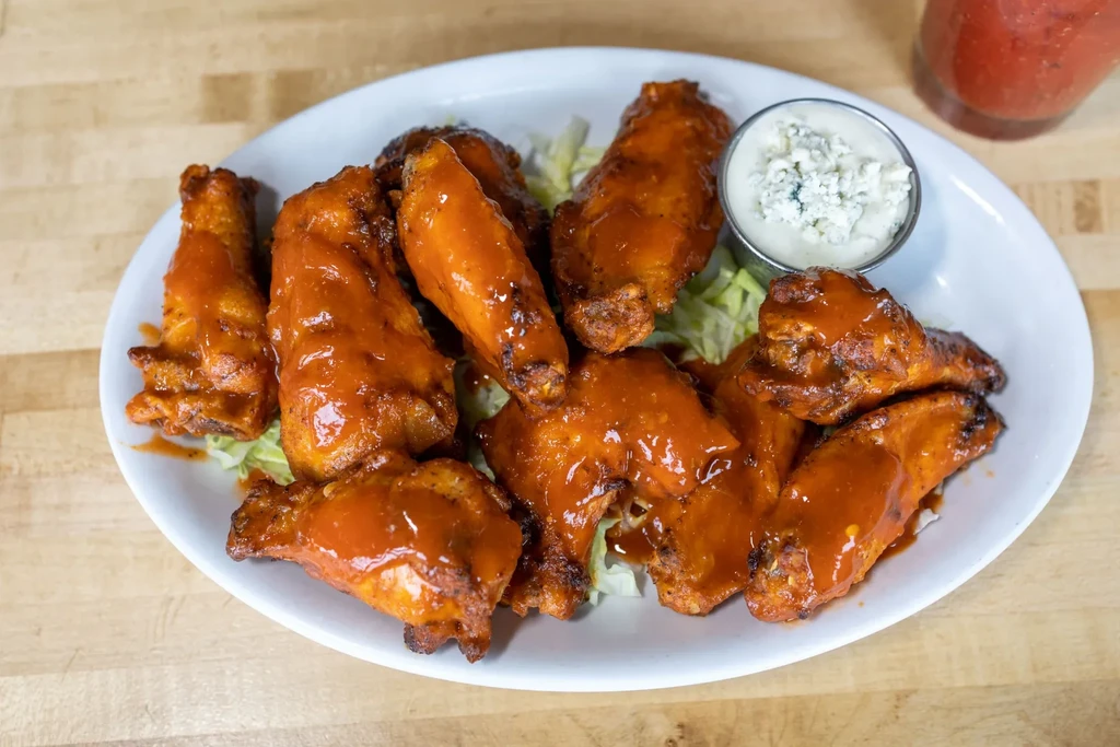 Buffalo chicken wings with blue cheese dressing, lettuce, on a white plate.