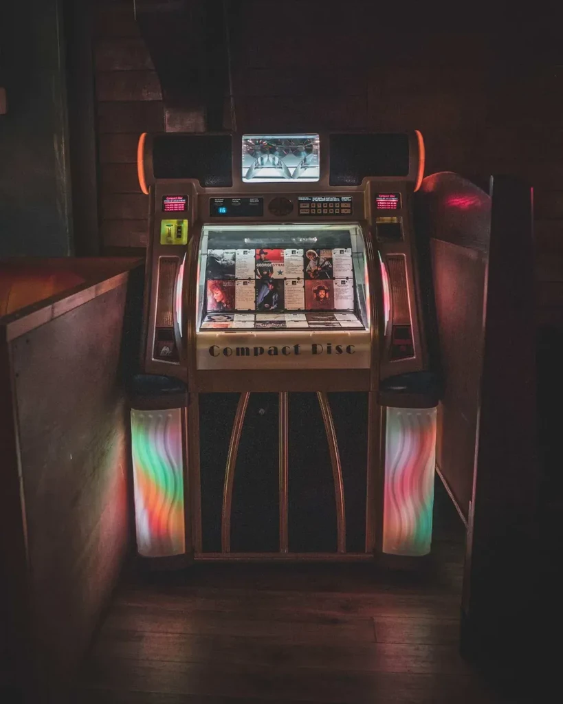 Vintage 'Compact Disc' jukebox, dimly lit, displays albums and colorful side lights.