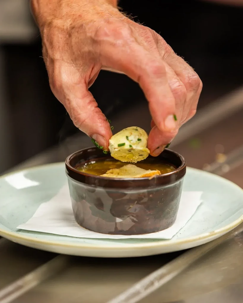 Close-up: Hand places herb-topped garnish into a steaming bowl of soup.