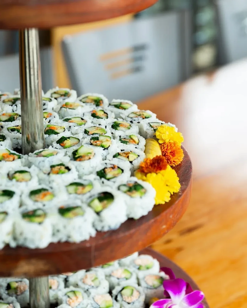 Abundant maki sushi rolls on a two-tiered wooden tray with flowers.