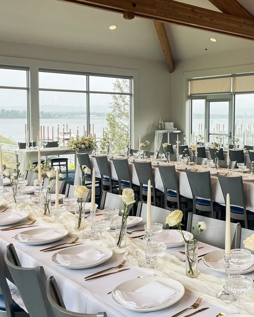 Elegant dining room with decorated tables, candles, white flowers, and water view.