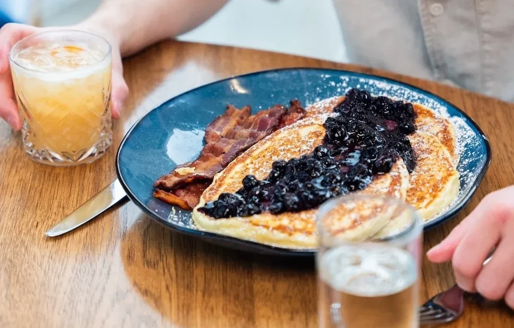 Blue plate of pancakes with blueberry compote, bacon, and drinks.