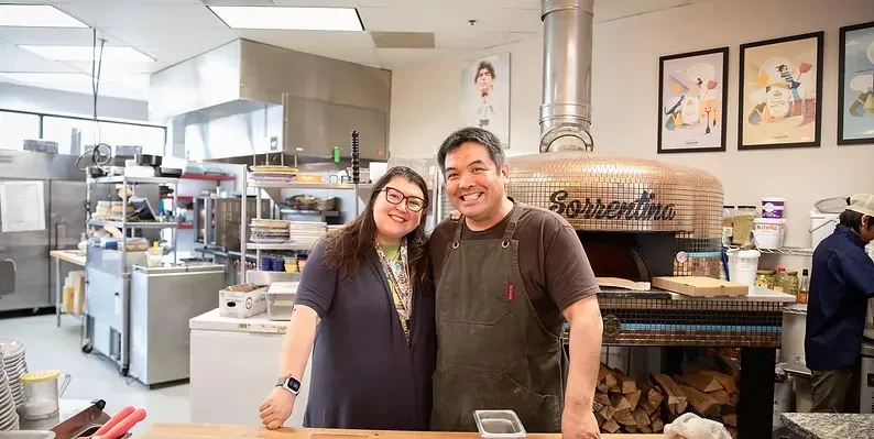 Two smiling people in a restaurant kitchen with Sorrentino pizza oven.