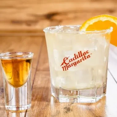 Cadillac Margarita with orange slice and a shot glass on wood.