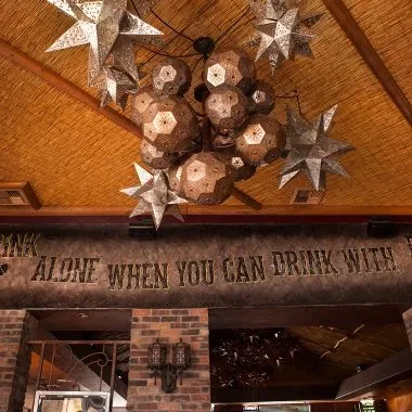 Upward view of ornate chandeliers, woven ceiling, and "DRINK ALONE" text.