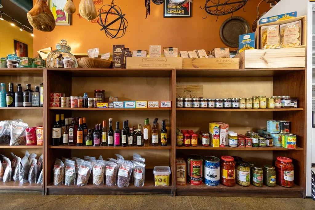 Warm-toned gourmet deli shelves displaying olive oils, pasta, and cured meats.