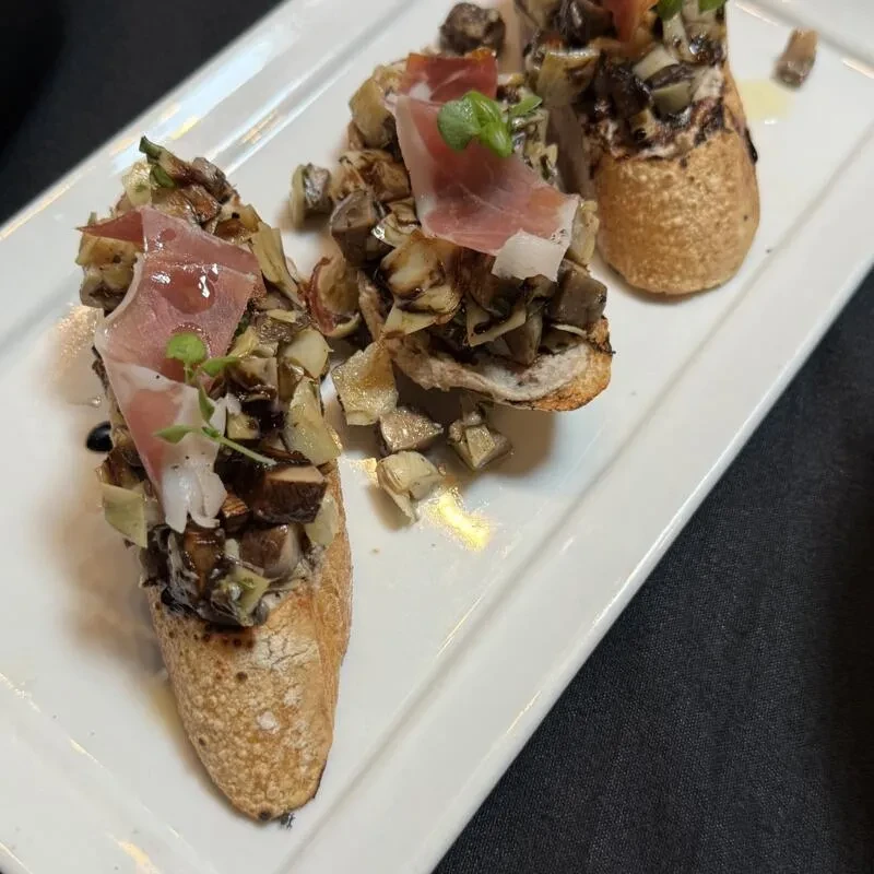 Three crostini appetizers topped with mushrooms, artichokes, prosciutto, herbs.