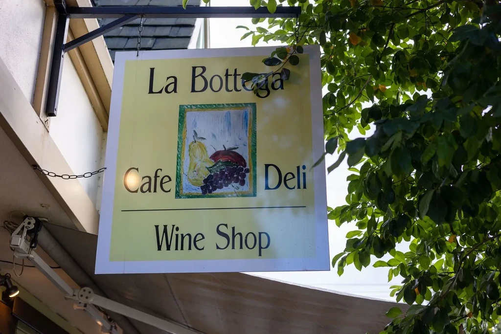 Hanging yellow sign for La Bottega Cafe, showing fruit still life.