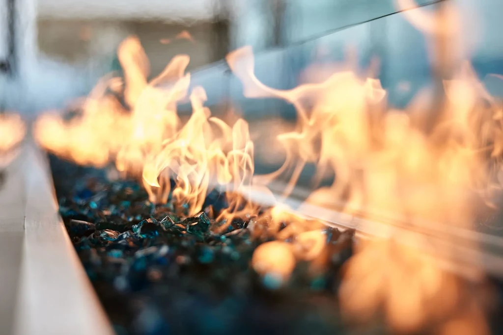 Modern gas fire pit with orange flames over blue glass beads.