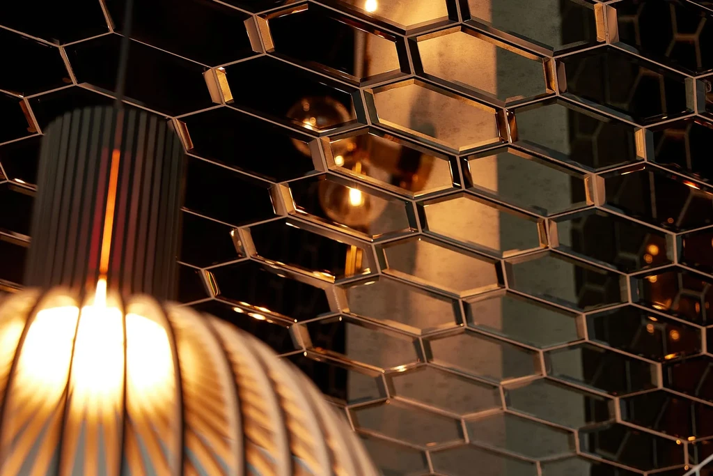 Textured lamp and hexagonal mirrored wall reflect warm light.