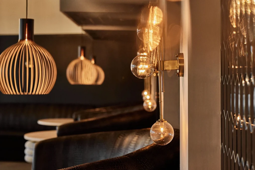 Warm restaurant interior with slatted wood pendants and dark booths.