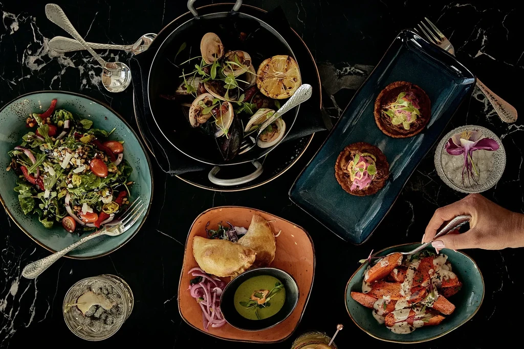 Overhead view: artfully arranged dishes, drinks, dark table, hand holding fork.
