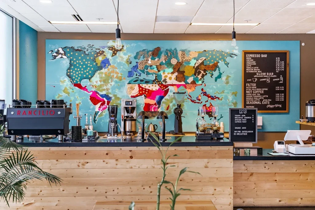 Coffee shop counter with espresso machine, equipment, and colorful world map mural.