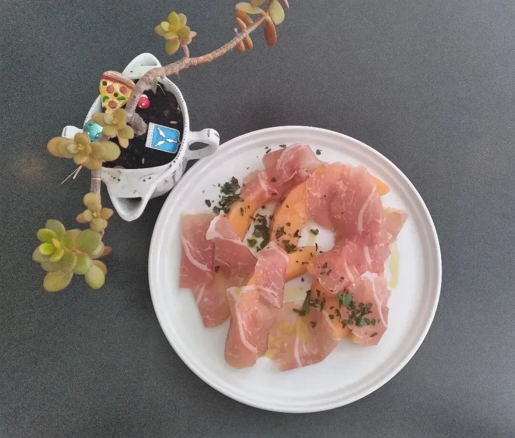 Top-down view of prosciutto and melon dish with herbs and succulent.