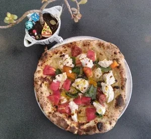 Fresh Neapolitan pizza, basil, tomatoes, mozzarella, next to a tiny decorated plant.