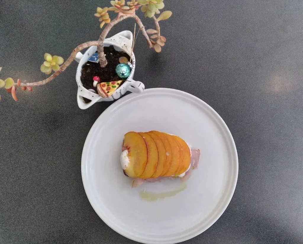 Prosciutto with peach slices and cream on a white plate.