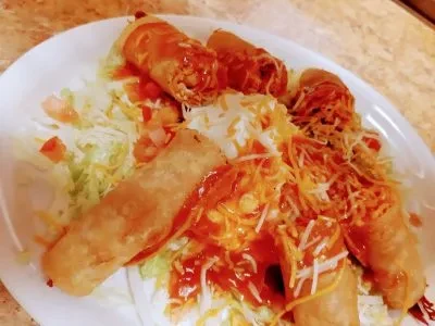 Golden taquitos with red sauce, cheese, sour cream, and lettuce.