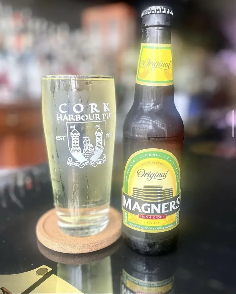 Condensation-covered Magners cider bottle and branded glass on bar.