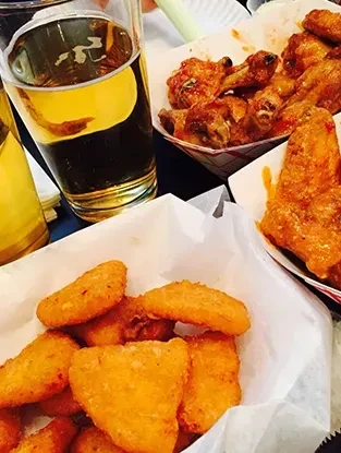 Overhead view of beer, fried food basket, and sauced chicken wings.