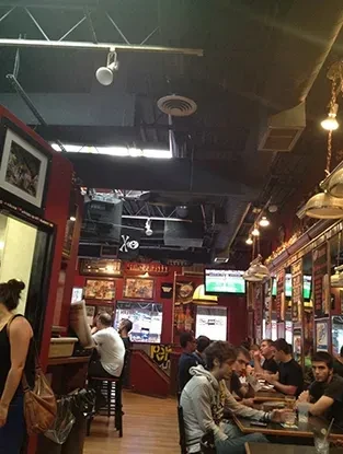 Lively red-walled pub interior with framed art, TVs, and exposed ducts.