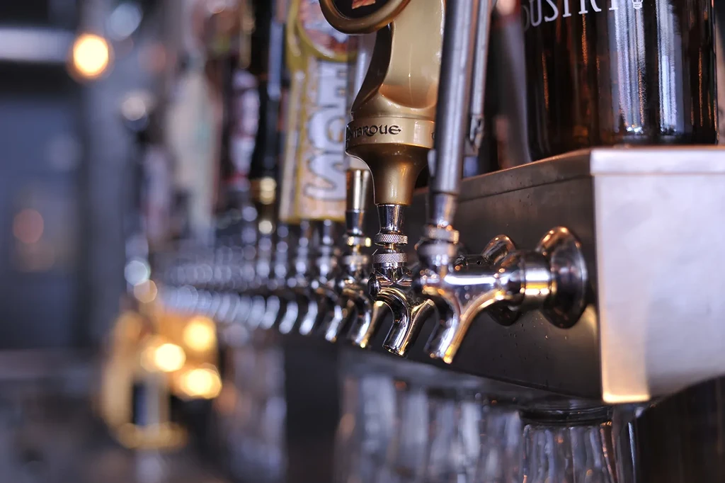 Row of chrome and brass beer tap handles in a bar.